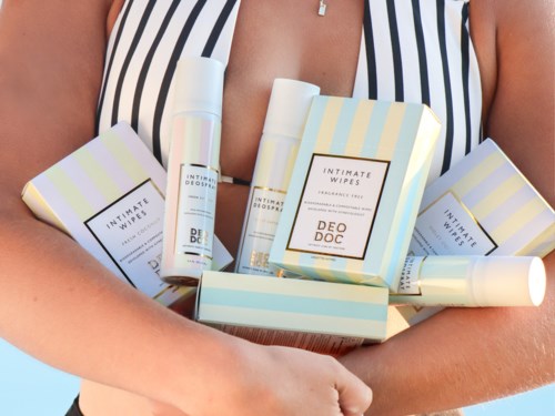 En kvinna i en randig klänning håller olika paket av intimservetter och deodorantprodukter.