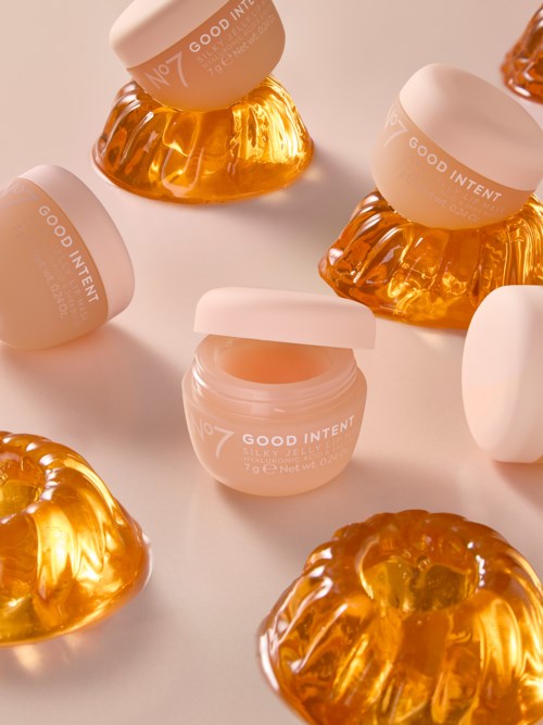 Kleine Gläser mit rosa Deckel und orangenen gelartigen Leckereien, auf einer weißen Oberfläche angeordnet.