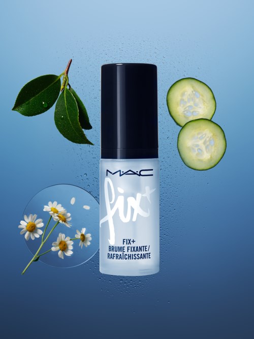 En MAC Fix+ sprayflaska omgiven av gurkskivor, kamomillblommor och gröna blad på en blå bakgrund.