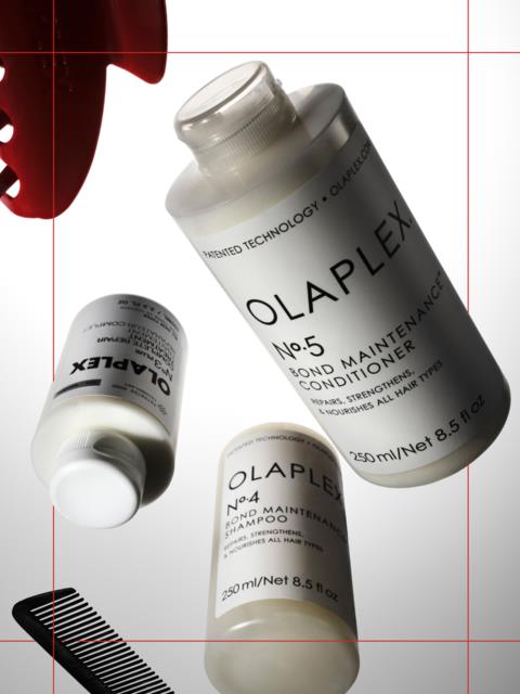 Tre flasker med Olaplex hårpleieprodukter vises, inkludert sjampo og balsam, med en kam i nærheten.