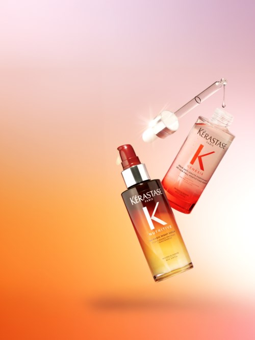 En Kerastase håroljeburk med dropper och en låda visas mot en mjuk orange-rosa bakgrund.