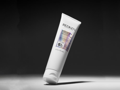 Redken hårprodukt i tub med vit kropp, lila och svart etikett, mot en mörk bakgrund.