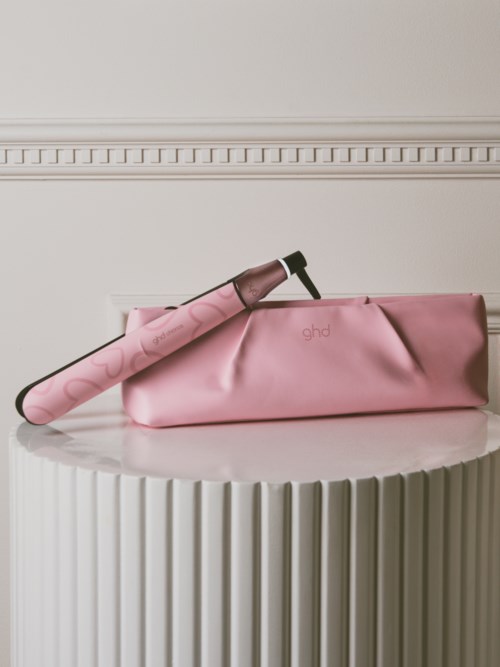A pink curling iron with a pink sleeve in a matching pink bag on a white round table.