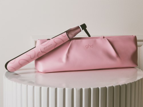 Pink reseväska med ghd-logga och en locktång på en vit texturerad yta.