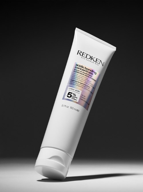 A white tube of Redken hair product with purple and black text on a dark background.