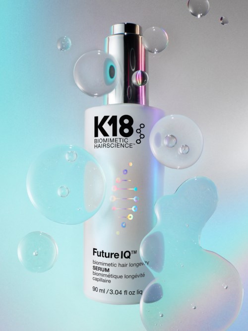 K18 Future IQ serum i vit flaska med färgglada prickar, omgivet av flytande bubblor, på en ljus gradientbakgrund.