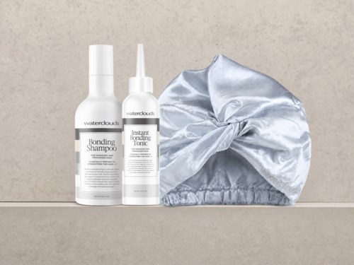 Två vita flaskor med hårvårdsprodukter, en märkt Bombing Shampoo och den andra Instant Bonding Tonic, bredvid en silverfärgad satinmössa.