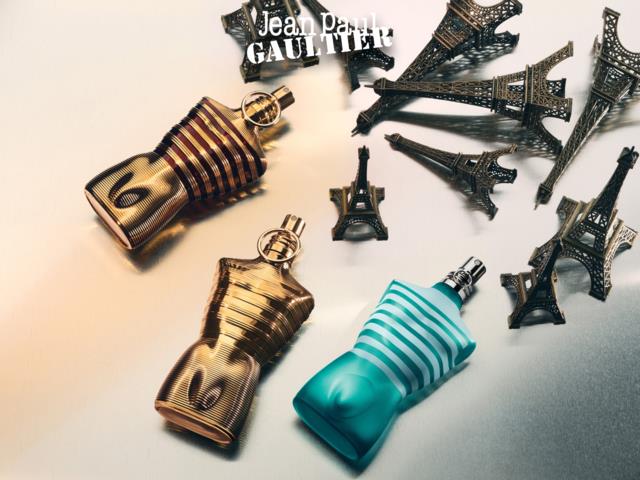 Tre parfymflaskor med metalliska ytor och en blå rutig flaska, omgivna av små Eiffel Tower-figurer och en Jean Paul Gaultier-logga.