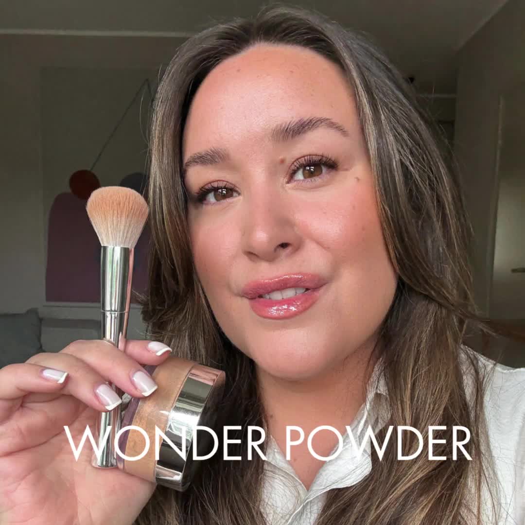En kvinna som håller en makeup-borste nära sitt ansikte, med texten "Wonder Powder."
